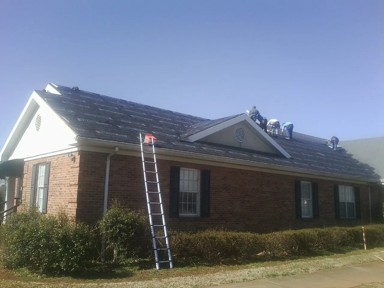 Crew tearing shingles off a brick ranch roof with a ladder set — Emergency Roof Repair work by our crew in Collinsville